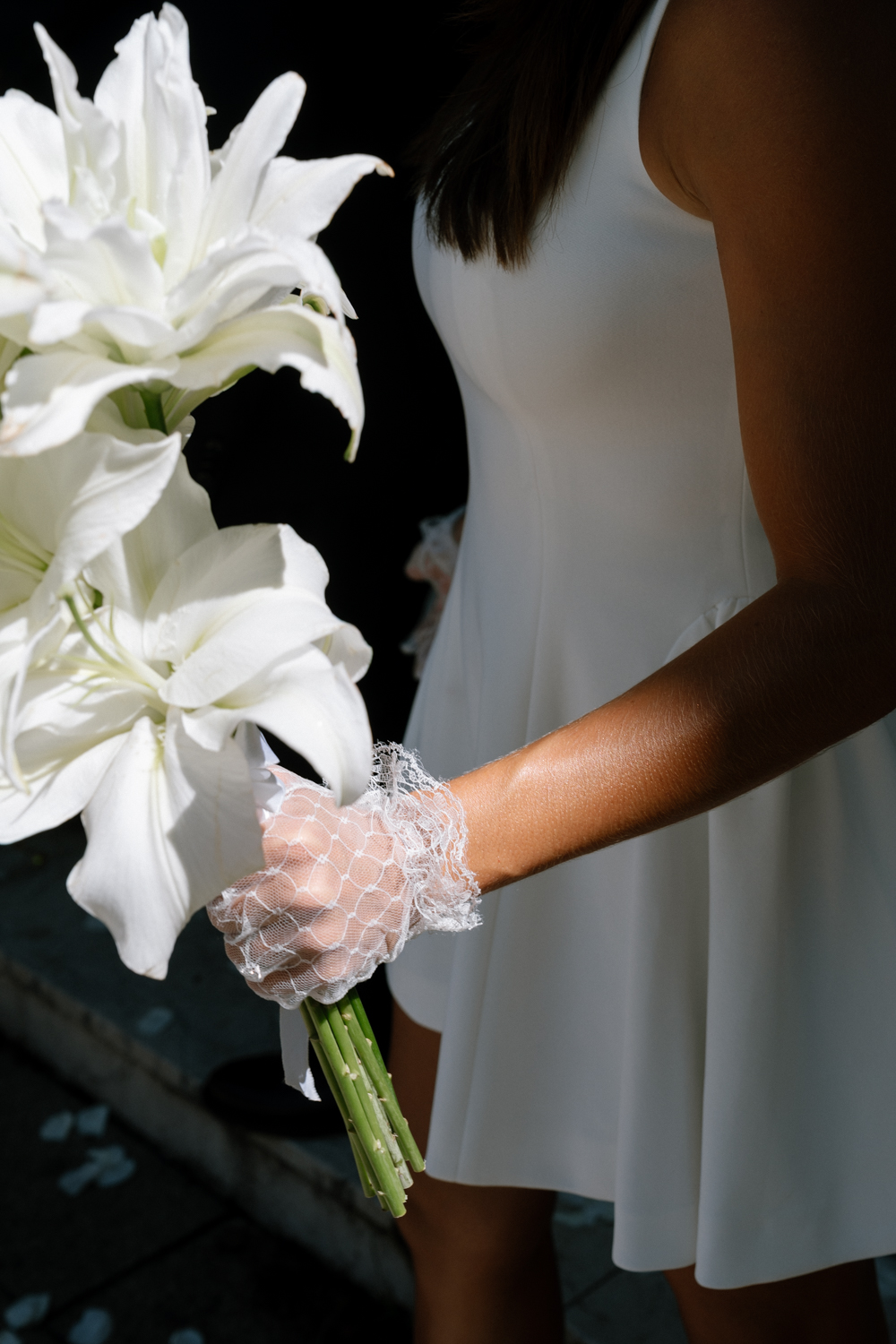 Mariée qui tient son bouquet à la sortie de la mairie, focus sur les mains avec son gant en dentelle